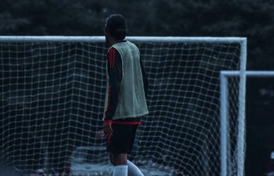 man in white shirt and black pants walking on soccer field during daytime
